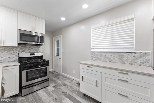 kitchen featuring appliances with stainless steel finishes, backsplash, white cabinetry, and light hardwood / wood-style flooring