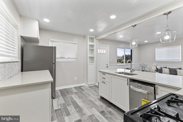 kitchen featuring white cabinets, light wood-type flooring, stainless steel appliances, sink, and pendant lighting