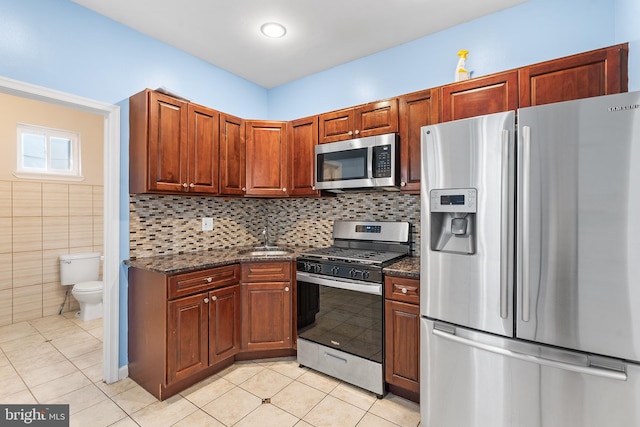 kitchen featuring dark stone countertops, stainless steel appliances, sink, decorative backsplash, and tile walls