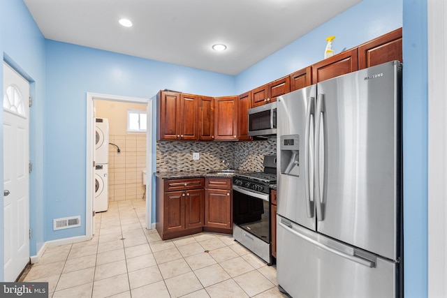 kitchen with stainless steel appliances, light tile patterned flooring, and stacked washing maching and dryer