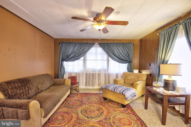 living room featuring light carpet, a textured ceiling, ceiling fan, and wooden walls