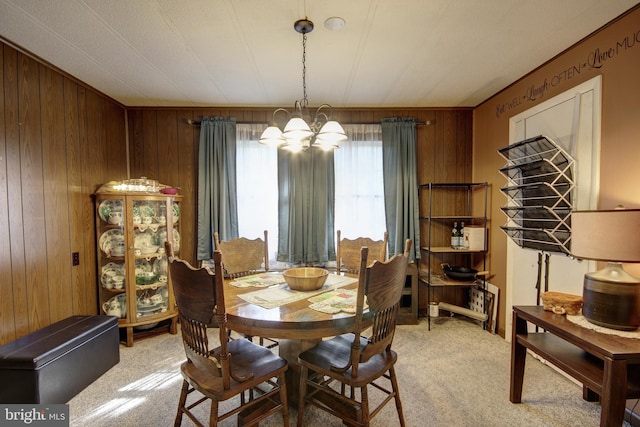 dining room featuring wood walls, light colored carpet, and an inviting chandelier