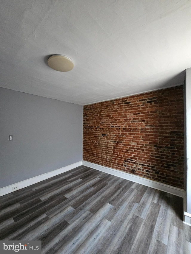 empty room featuring brick wall and dark hardwood / wood-style floors