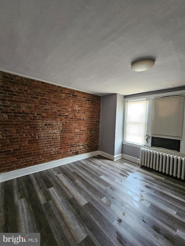 spare room featuring brick wall, dark wood-type flooring, a textured ceiling, and radiator