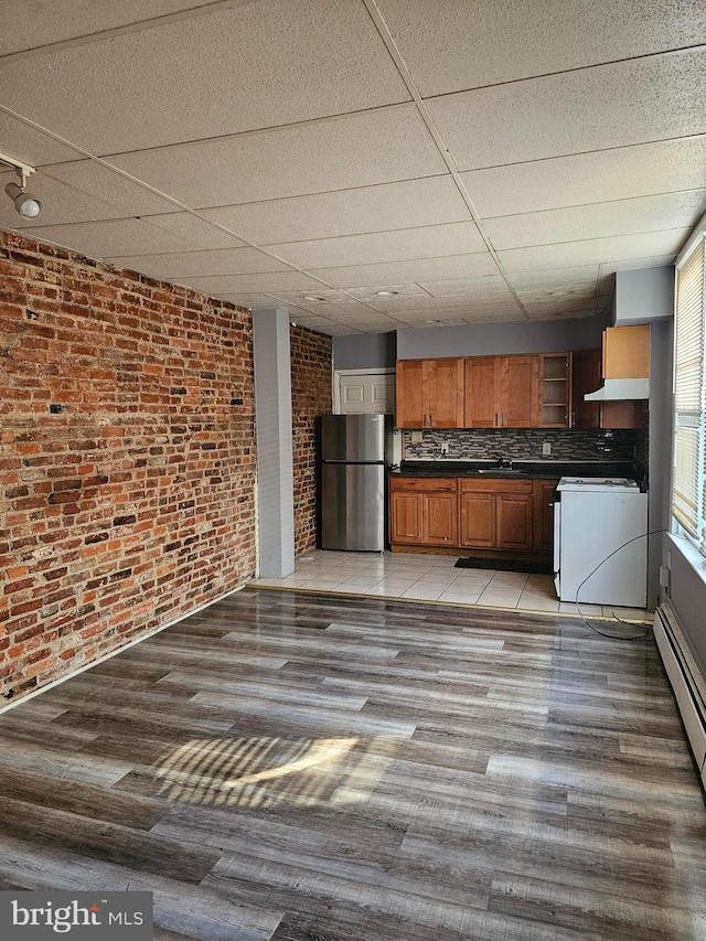 kitchen featuring decorative backsplash, white range, light wood-type flooring, stainless steel refrigerator, and brick wall