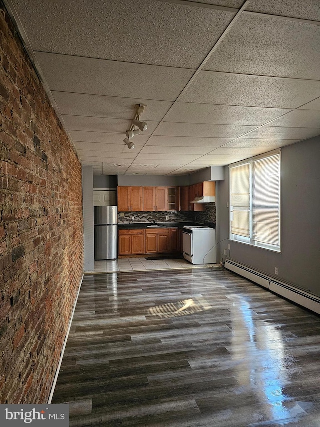 kitchen featuring backsplash, stainless steel fridge, white range with electric stovetop, dark wood-type flooring, and brick wall