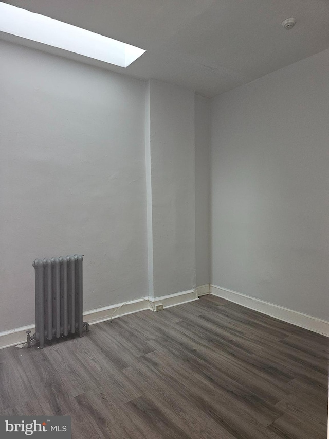 unfurnished room featuring a skylight, radiator heating unit, and dark hardwood / wood-style floors