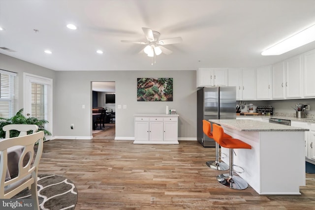 kitchen featuring light hardwood / wood-style floors, white cabinets, a kitchen island, stainless steel refrigerator, and ceiling fan