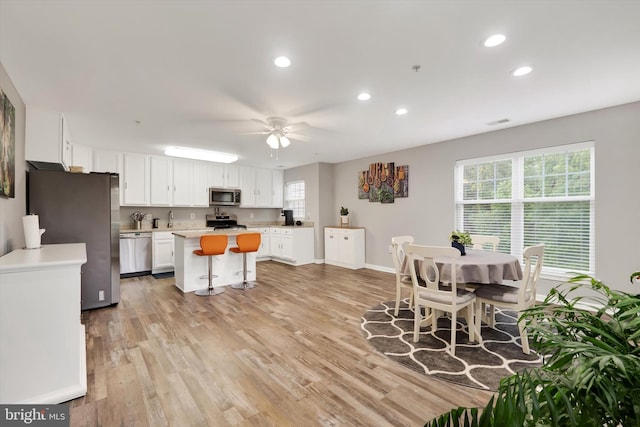 kitchen with a breakfast bar, white cabinets, light hardwood / wood-style flooring, appliances with stainless steel finishes, and ceiling fan