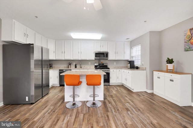 kitchen with appliances with stainless steel finishes, white cabinets, a kitchen island, a kitchen bar, and hardwood / wood-style flooring