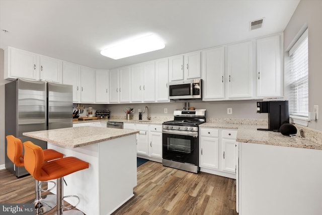 kitchen with light stone counters, light hardwood / wood-style flooring, appliances with stainless steel finishes, and white cabinetry