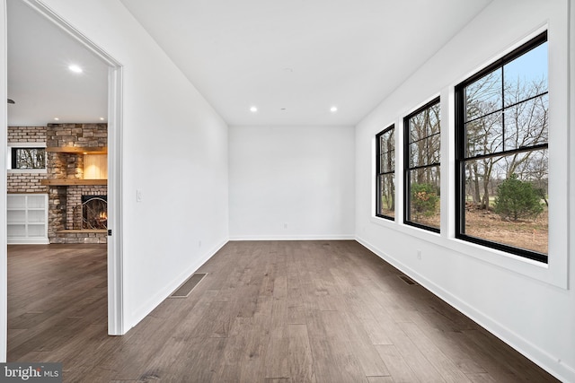 empty room with dark wood-type flooring, a wealth of natural light, a fireplace, and brick wall