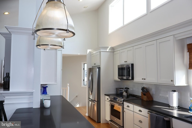 kitchen featuring decorative light fixtures, stainless steel appliances, light hardwood / wood-style floors, and white cabinetry