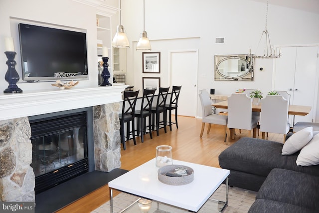 living room featuring a chandelier, light hardwood / wood-style floors, and a stone fireplace