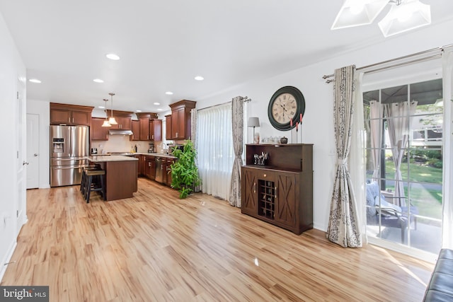 kitchen with appliances with stainless steel finishes, a kitchen breakfast bar, a kitchen island, light wood-type flooring, and decorative light fixtures