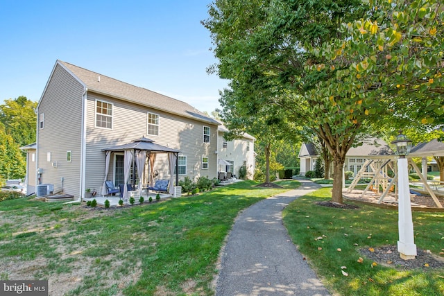 rear view of property featuring a playground, a gazebo, a yard, and central AC unit