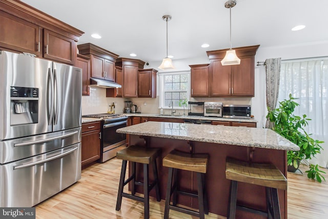 kitchen with stainless steel appliances, light wood-type flooring, a center island, decorative light fixtures, and sink