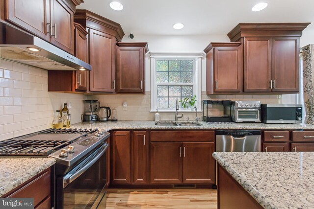 kitchen with light stone counters, light hardwood / wood-style floors, tasteful backsplash, sink, and appliances with stainless steel finishes