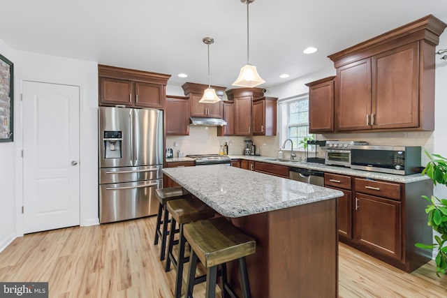 kitchen with pendant lighting, sink, a kitchen island, light hardwood / wood-style flooring, and stainless steel appliances