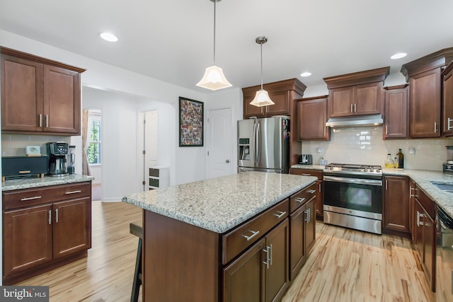 kitchen featuring light stone counters, hanging light fixtures, stainless steel appliances, a center island, and light wood-type flooring