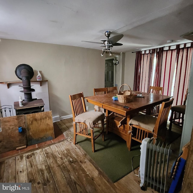 dining space featuring a wood stove, wood-type flooring, radiator, and ceiling fan