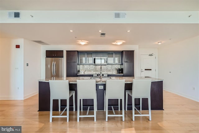 kitchen with light stone counters, a kitchen island with sink, stainless steel appliances, and a kitchen bar