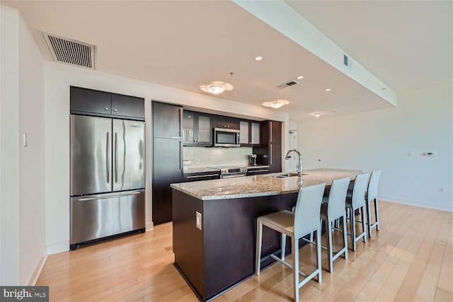 kitchen featuring an island with sink, sink, stainless steel appliances, light stone countertops, and a kitchen bar