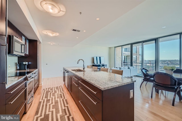 kitchen with appliances with stainless steel finishes, tasteful backsplash, light hardwood / wood-style flooring, a kitchen island with sink, and sink