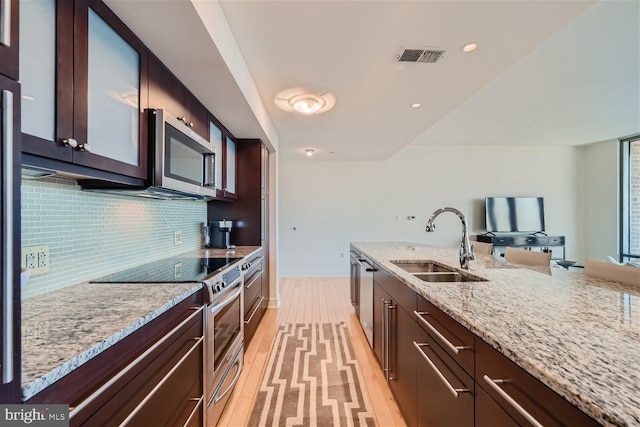 kitchen with appliances with stainless steel finishes, decorative backsplash, light stone counters, light hardwood / wood-style flooring, and sink