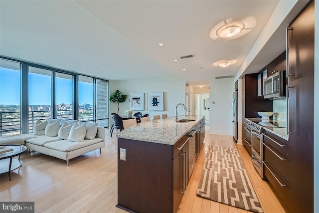 kitchen featuring an island with sink, stainless steel appliances, light stone counters, and light hardwood / wood-style flooring