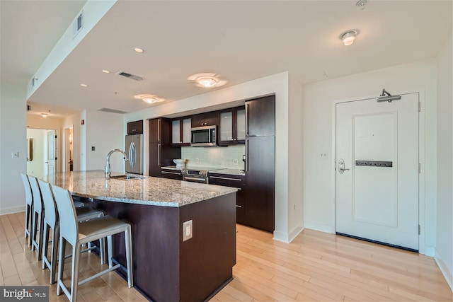 kitchen with a center island with sink, stainless steel appliances, a kitchen breakfast bar, light hardwood / wood-style floors, and decorative backsplash