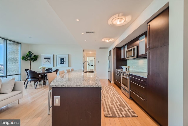 kitchen featuring appliances with stainless steel finishes, light hardwood / wood-style floors, an island with sink, a breakfast bar, and sink