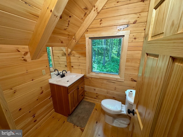 half bathroom featuring toilet, vanity, wooden walls, and wood finished floors