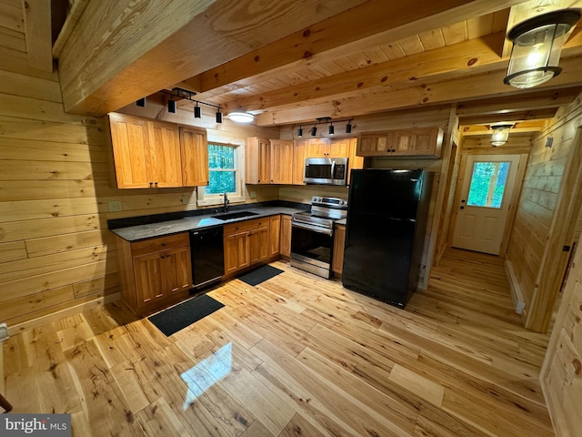 kitchen with black appliances, light wood-style flooring, wood walls, and a sink