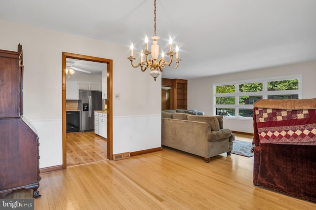 living room with ceiling fan with notable chandelier and light hardwood / wood-style floors