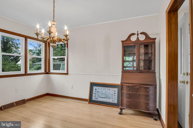 empty room with a notable chandelier, light hardwood / wood-style floors, and ornamental molding