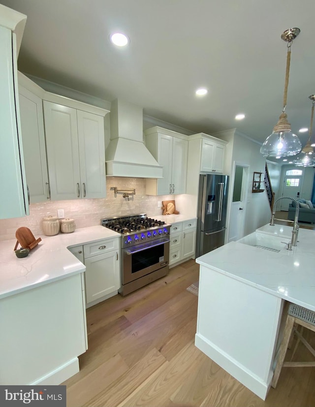 kitchen featuring premium range hood, decorative light fixtures, white cabinetry, appliances with stainless steel finishes, and light hardwood / wood-style floors