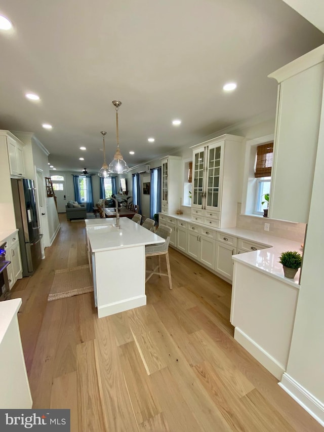 kitchen with pendant lighting, light hardwood / wood-style floors, an island with sink, stainless steel refrigerator with ice dispenser, and white cabinetry