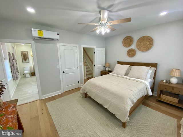 bedroom featuring an AC wall unit, wood-type flooring, ceiling fan, and ensuite bathroom