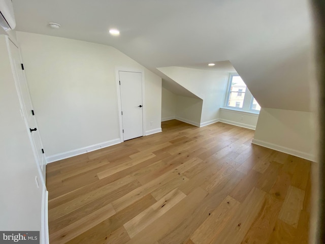 additional living space featuring light wood-type flooring, lofted ceiling, and a wall mounted air conditioner