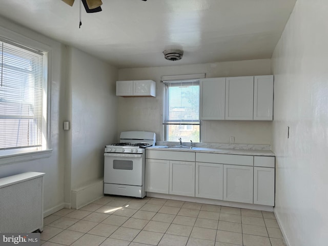 kitchen with white range with gas stovetop, white cabinets, ceiling fan, and a wealth of natural light