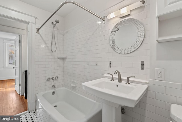 bathroom with hardwood / wood-style flooring, toilet, tile walls, and tiled shower / bath combo