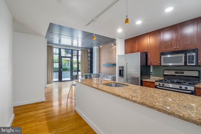 kitchen with appliances with stainless steel finishes, light wood-type flooring, track lighting, decorative light fixtures, and sink