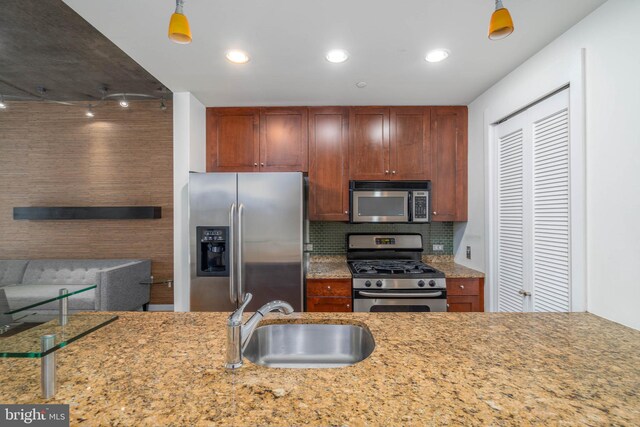 kitchen with light stone counters, sink, tasteful backsplash, decorative light fixtures, and stainless steel appliances