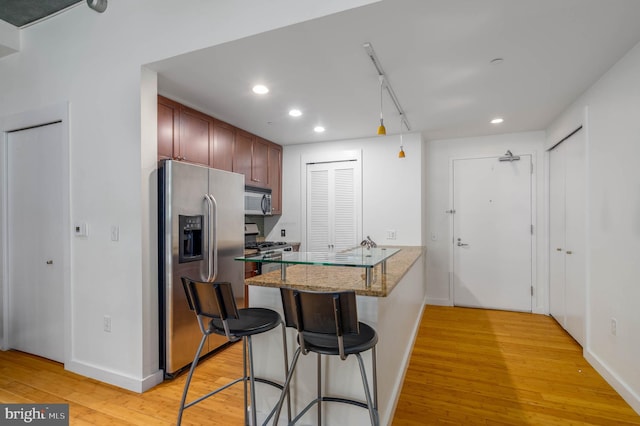 kitchen featuring light hardwood / wood-style floors, kitchen peninsula, stone counters, appliances with stainless steel finishes, and a kitchen bar