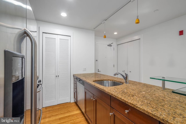 kitchen featuring appliances with stainless steel finishes, hanging light fixtures, light stone countertops, light hardwood / wood-style flooring, and sink