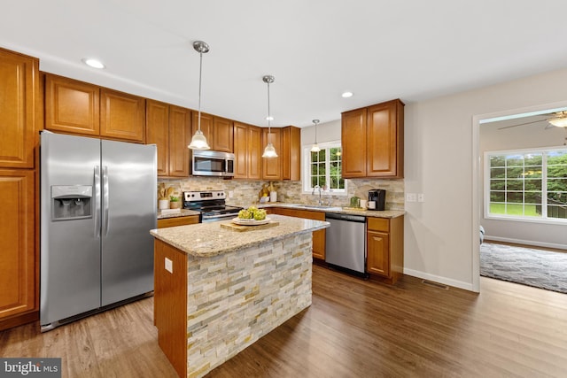 kitchen featuring light stone counters, pendant lighting, a kitchen island, hardwood / wood-style flooring, and appliances with stainless steel finishes