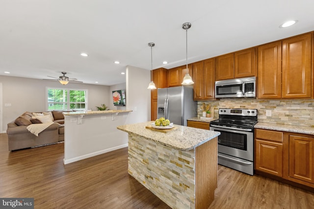 kitchen featuring pendant lighting, appliances with stainless steel finishes, hardwood / wood-style floors, light stone countertops, and ceiling fan