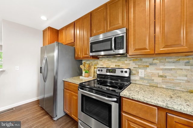 kitchen with light hardwood / wood-style flooring, appliances with stainless steel finishes, light stone countertops, and tasteful backsplash