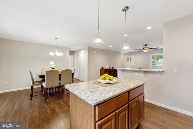 kitchen with a center island, hardwood / wood-style flooring, ceiling fan with notable chandelier, hanging light fixtures, and light stone countertops